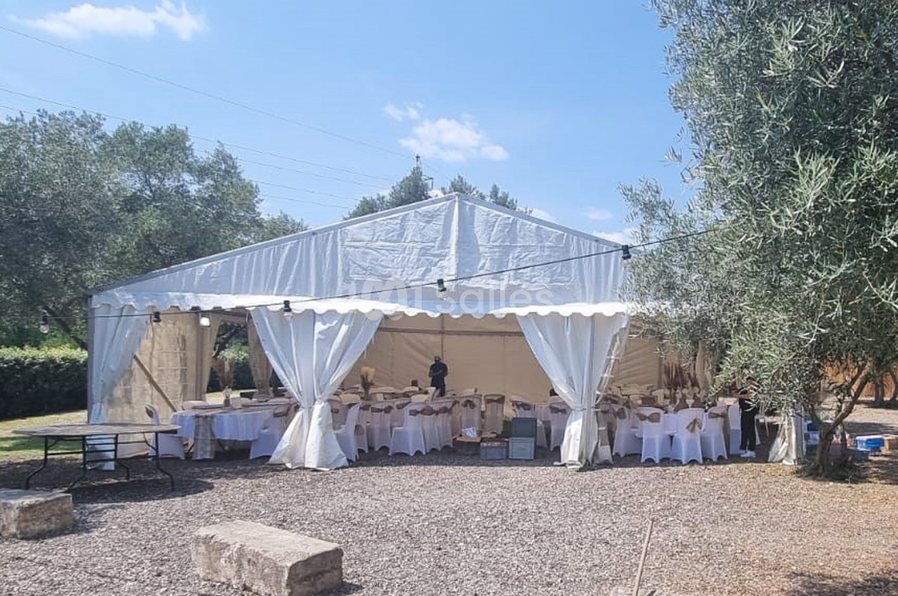 Tente blanche installée en extérieur, aménagée avec des tables et chaises pour un événement.