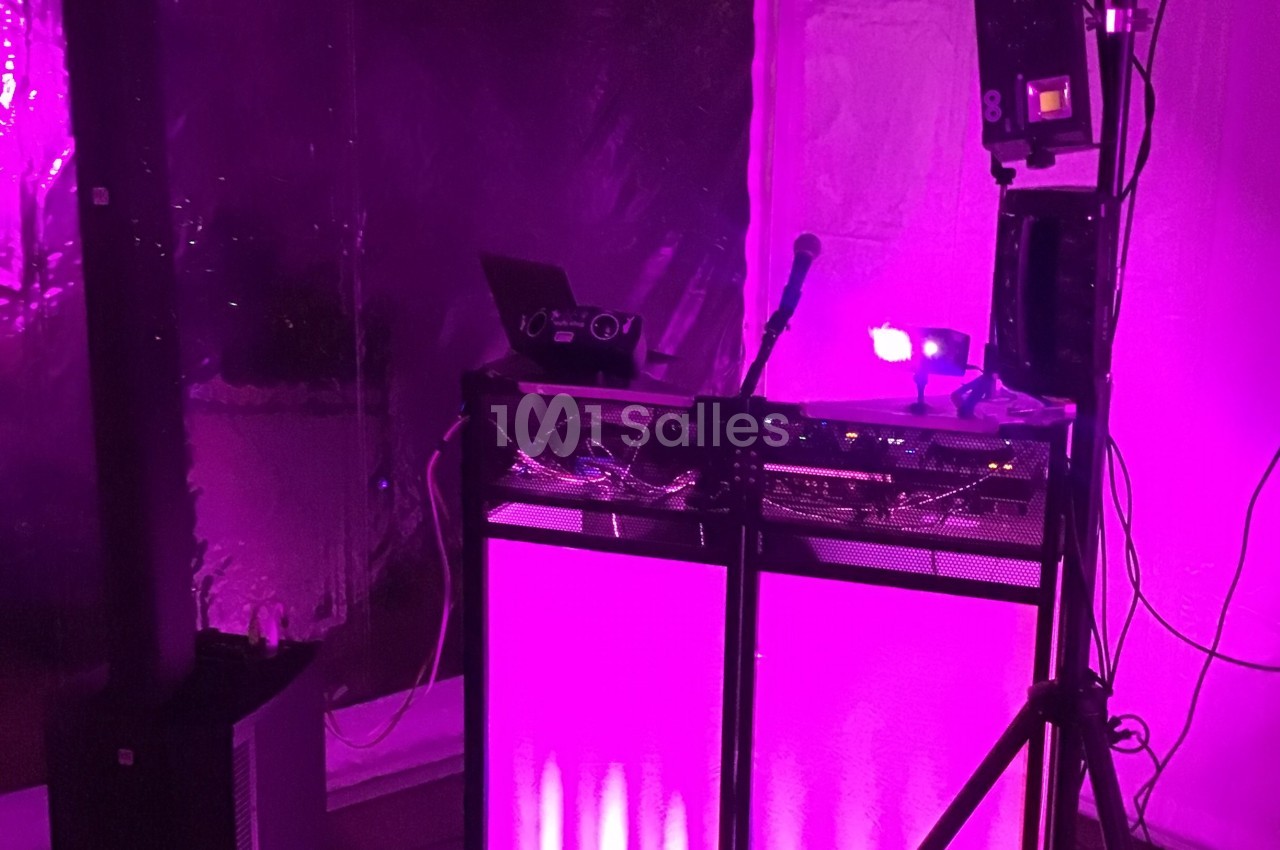Poste de DJ éclairé par une lumière rose, avec un micro, un ordinateur portable et du matériel audio.