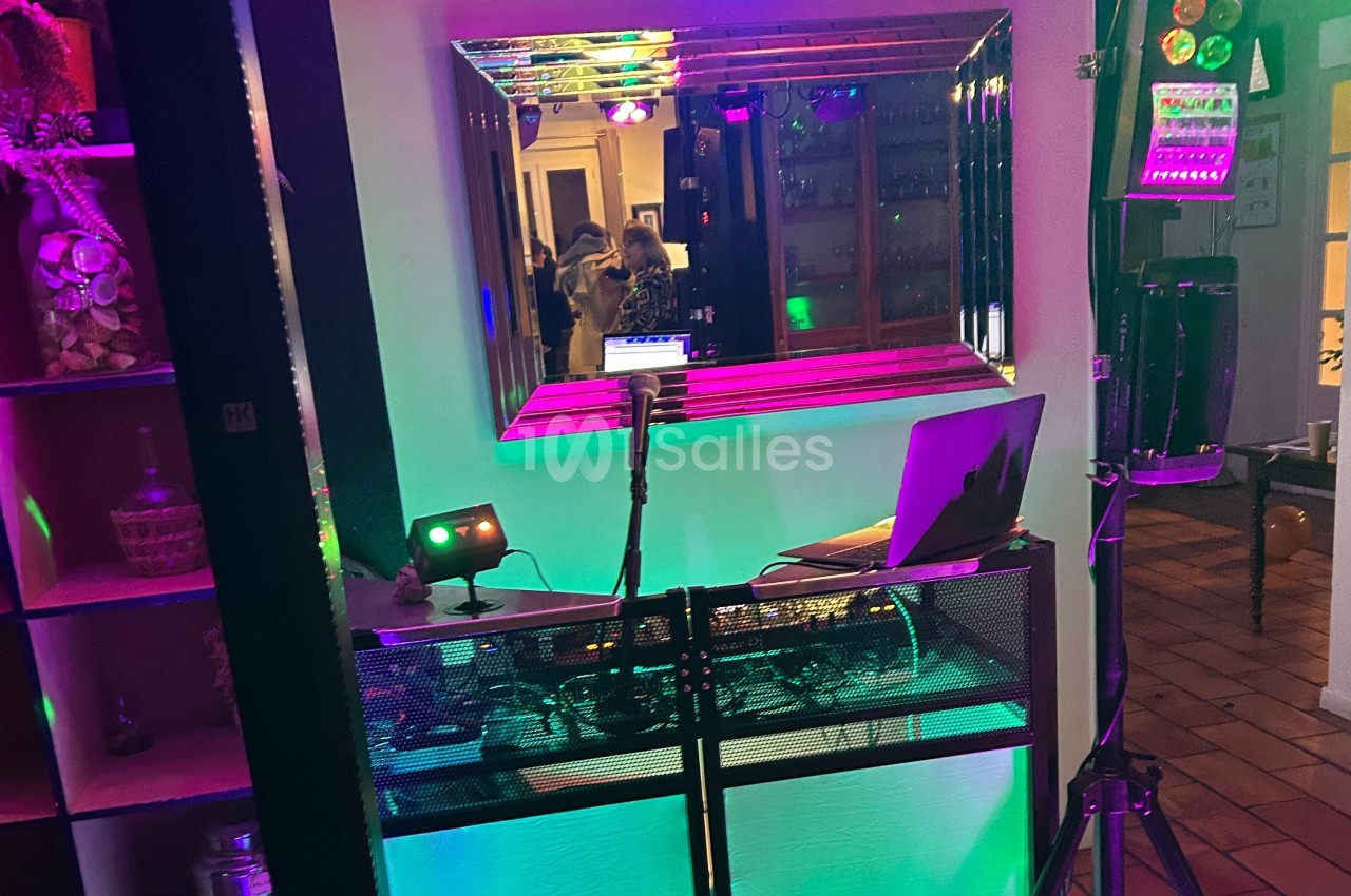 Poste de DJ avec ordinateur portable, microphone et éclairage coloré, installé devant un miroir dans un espace intérieur.