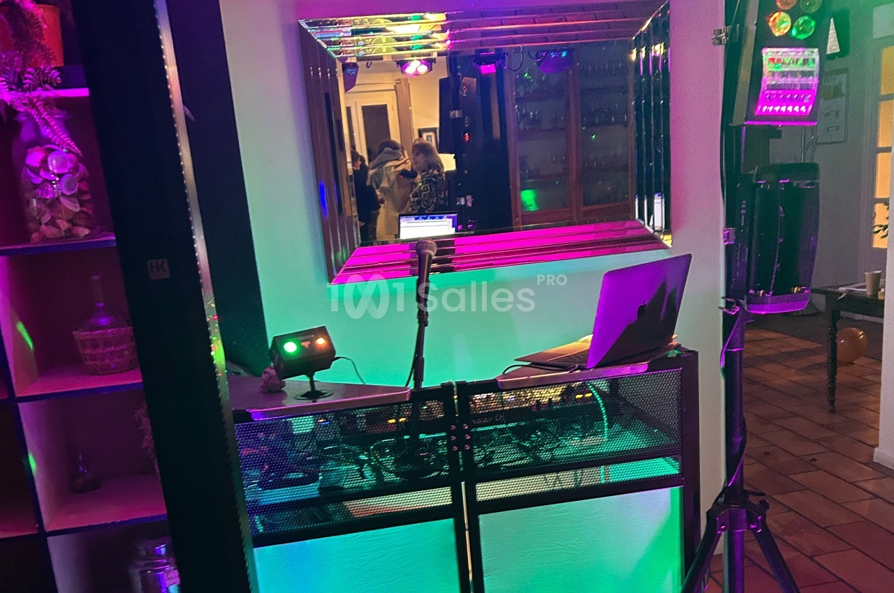 Poste de DJ avec ordinateur portable, micro et éclairage coloré, reflété dans un miroir dans un espace intérieur.