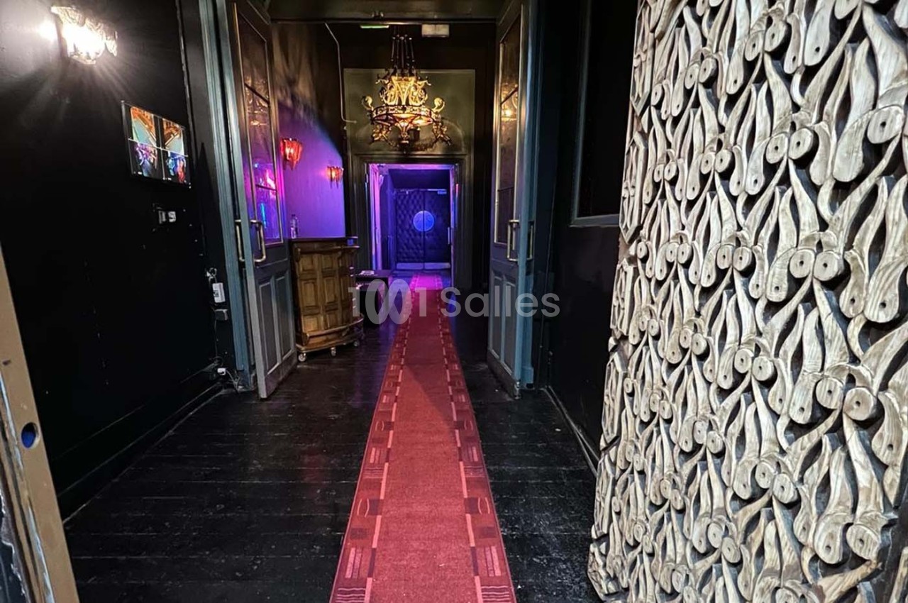 Couloir sombre avec tapis rouge, éclairage tamisé, lustre suspendu et décorations murales sculptées.