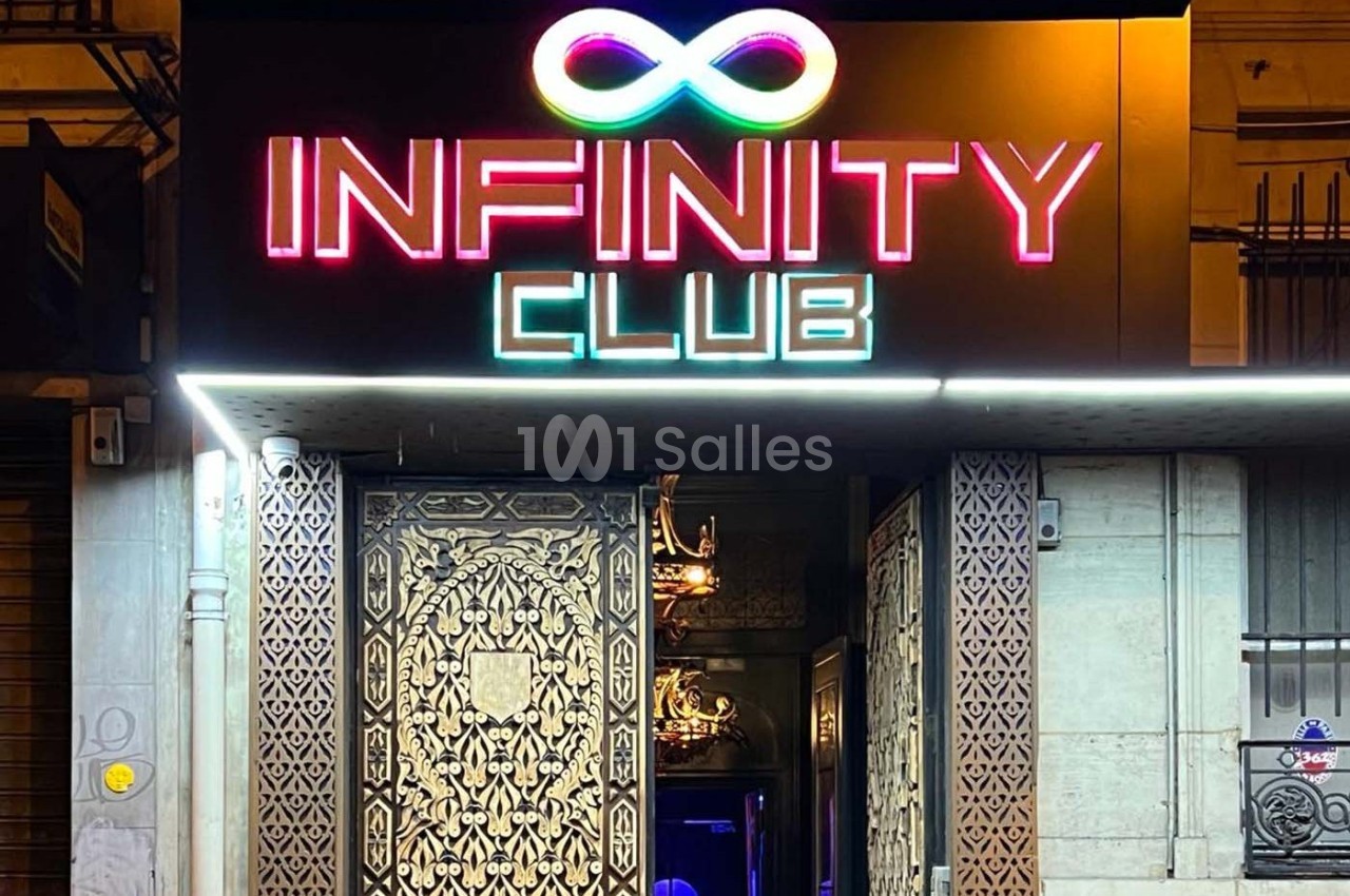Entrée d'un club nocturne avec enseigne lumineuse ’Infinity Club’ et porte ornée de motifs décoratifs.
