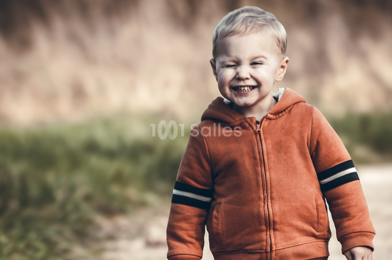 Un enfant souriant portant un sweat à capuche orange marche sur un chemin en plein air.