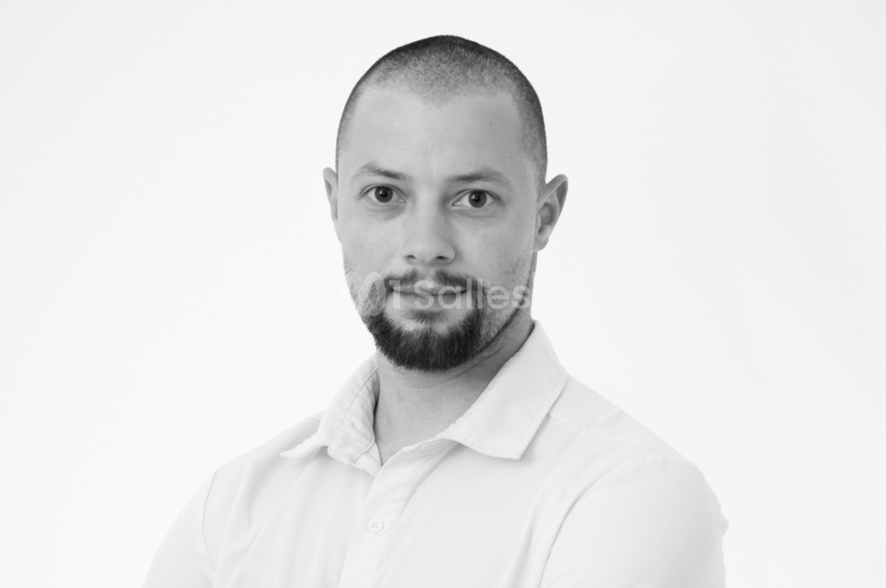 Portrait en noir et blanc d'un homme au crâne rasé et barbe, portant une chemise claire, regardant vers l'objectif.