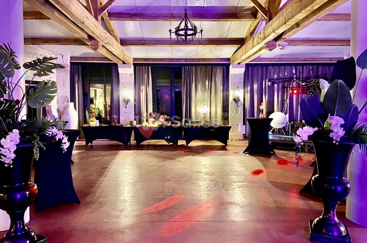 Salle de réception décorée avec des plantes, des tables drapées et un éclairage tamisé dans une ambiance festive.