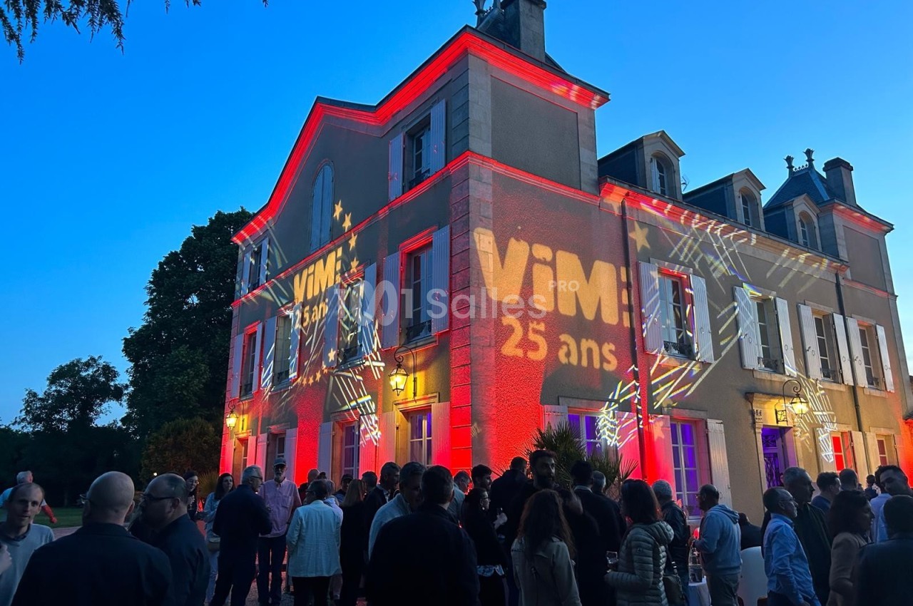 Façade d'un bâtiment illuminée par des projections lumineuses, avec une foule rassemblée devant au crépuscule.
