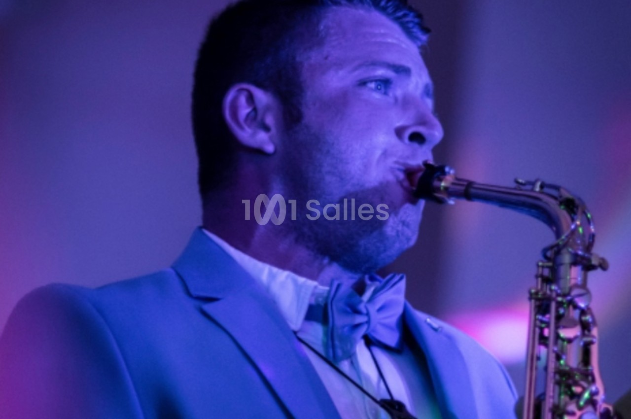 Homme en costume jouant du saxophone sous un éclairage violet.