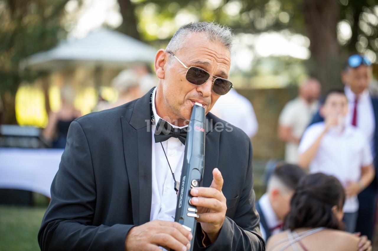 Un homme en costume joue d'un instrument à vent électronique lors d'un événement en plein air.