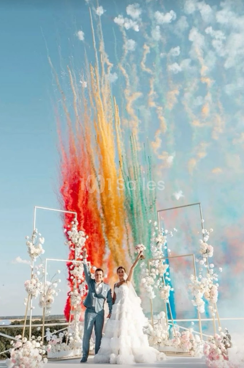 Un couple en tenue de mariage célèbre sous des feux d'artifice colorés, entouré de décorations florales.
