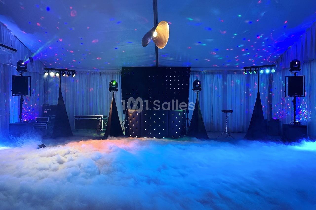 Salle de réception avec éclairage coloré, piste de danse entourée de fumée et équipement de sonorisation.