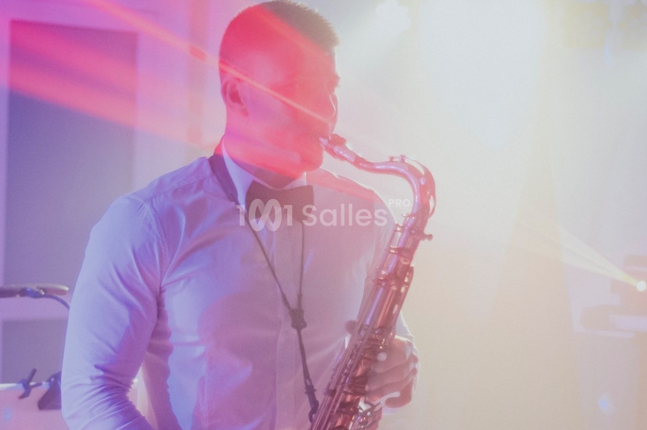 Un musicien en chemise blanche et nœud papillon joue du saxophone sous des lumières colorées.