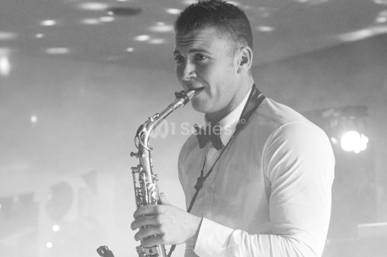 Un musicien en chemise blanche et nœud papillon joue du saxophone dans une ambiance tamisée.