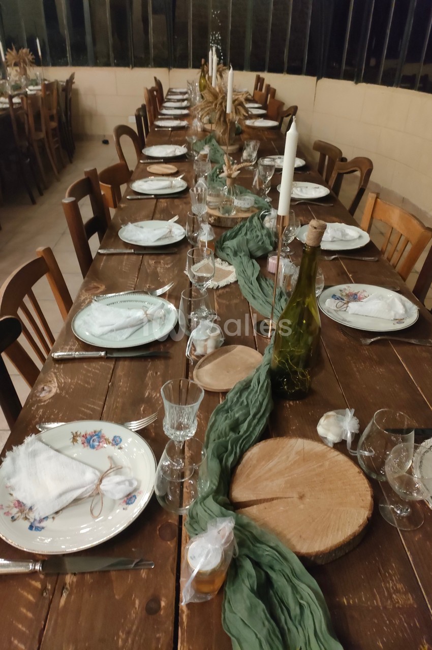 Table en bois rustique dressée pour un repas, avec vaisselle, bougies, rondins décoratifs et chemin de table vert.