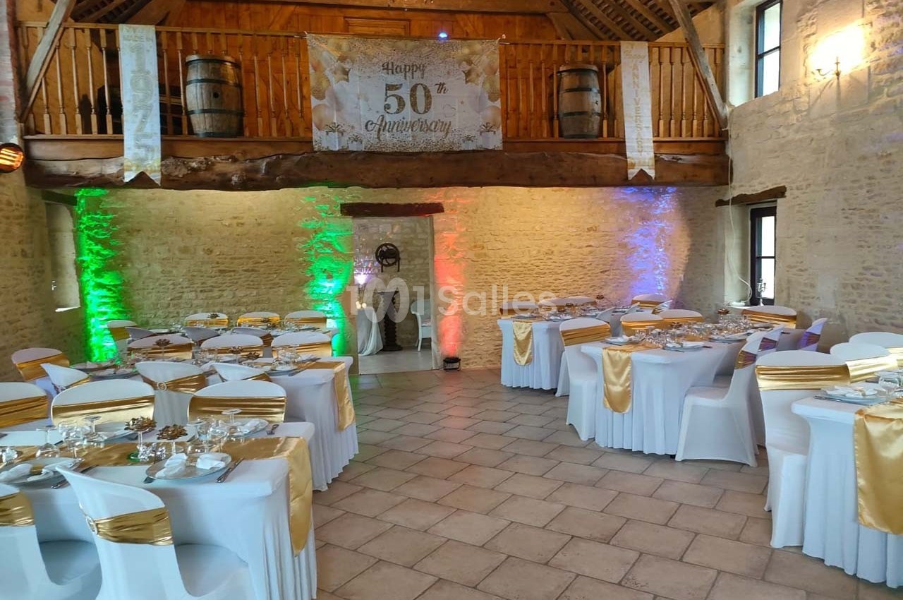 Salle de réception décorée pour un 50e anniversaire, avec tables dressées et éclairage coloré.