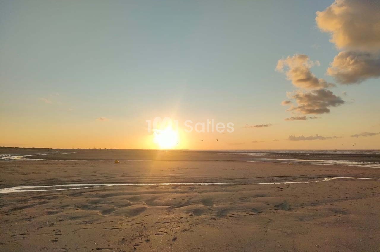 Coucher de soleil sur une plage avec des nuages légers, des reflets sur le sable et des ruisseaux d'eau.