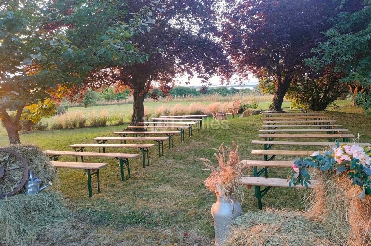 Bancs en bois disposés en rangées dans un jardin verdoyant, entourés d'arbres et de décorations champêtres.