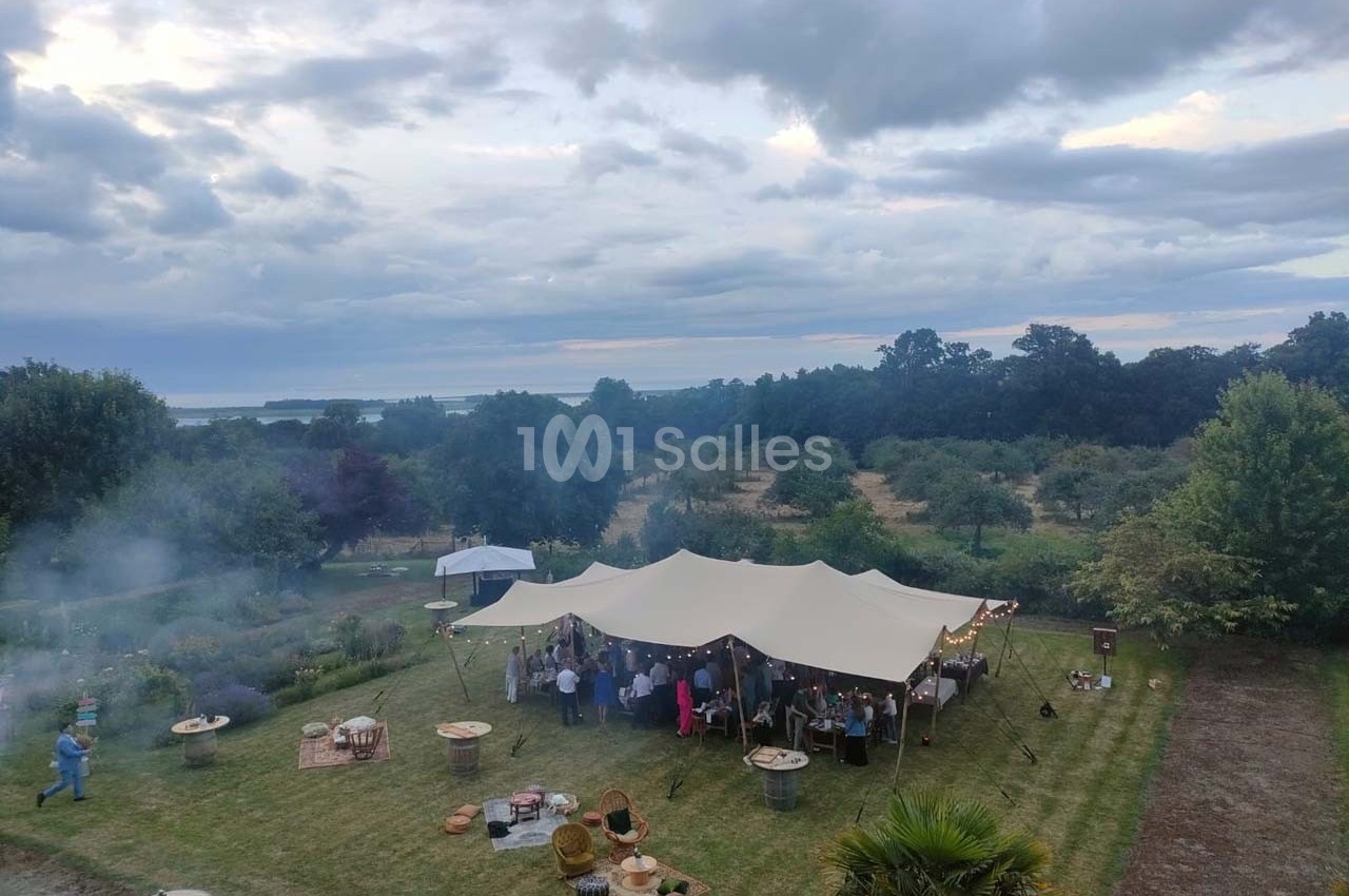 Tente blanche abritant un rassemblement en plein air dans un jardin verdoyant sous un ciel nuageux.