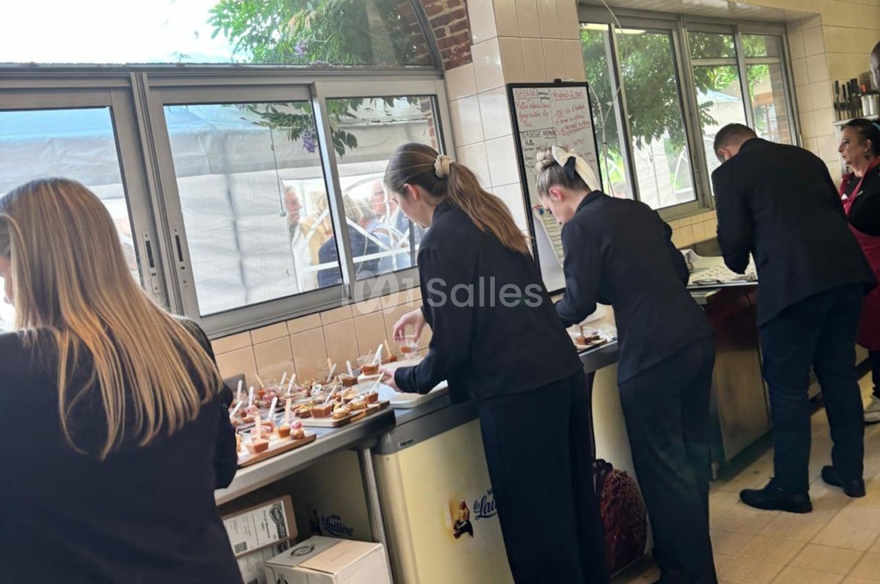 Des serveurs en tenue professionnelle préparent des plateaux de bouchées dans une cuisine lumineuse.