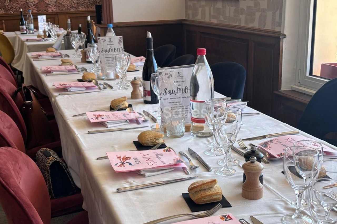 Table dressée pour un repas, avec nappes blanches, assiettes, verres, bouteilles d'eau et de vin, et menus disposés.