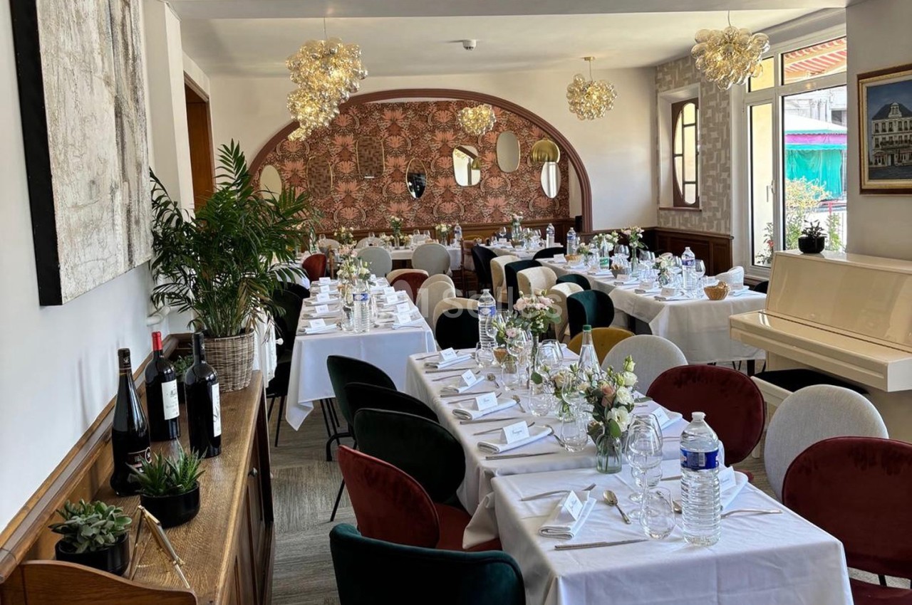 Salle de restaurant élégamment décorée avec des tables dressées, des chaises colorées et des luminaires suspendus.