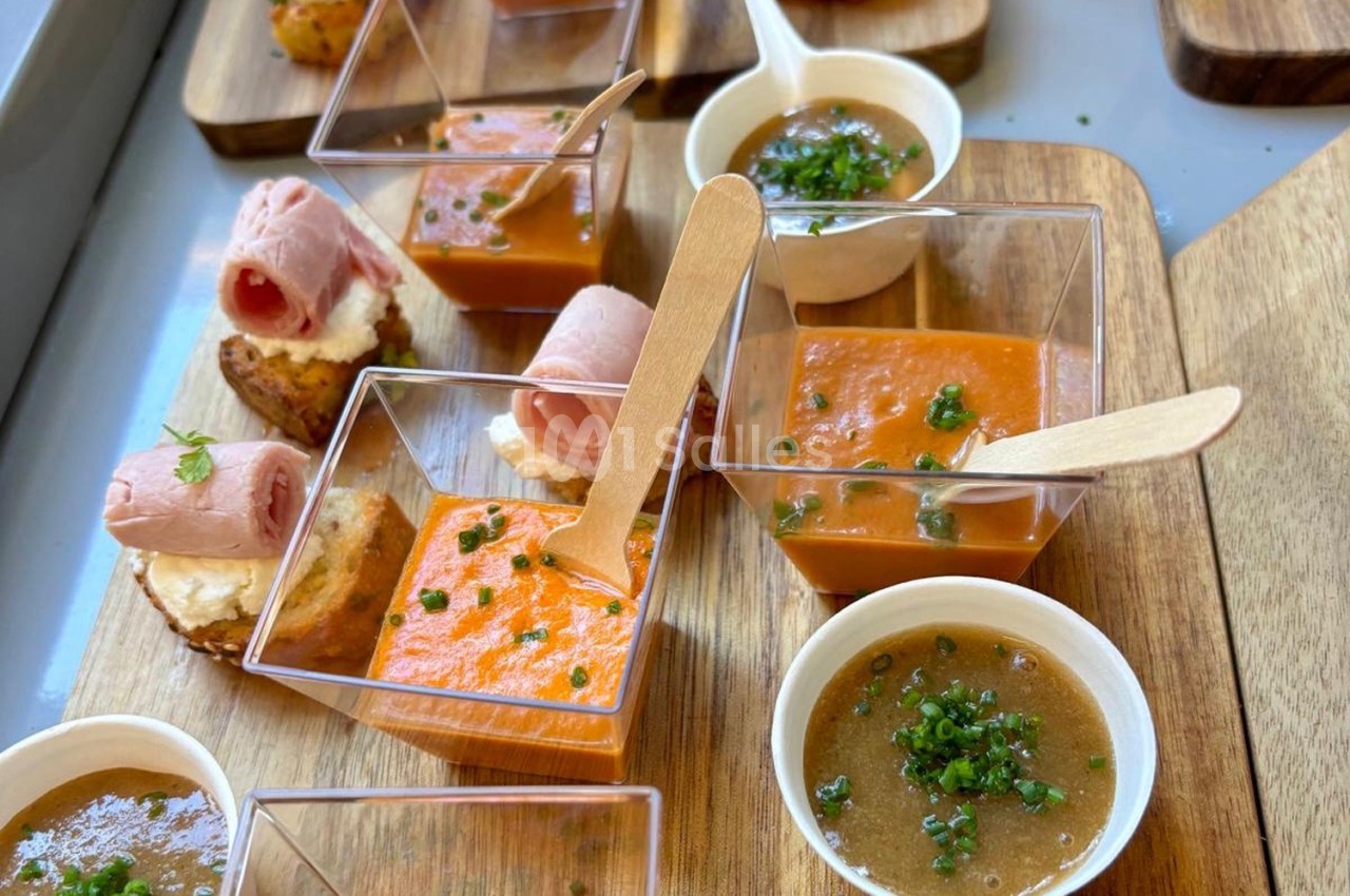 Assortiment de verrines de soupe, toasts au jambon et petites sauces, présenté sur des planches en bois.