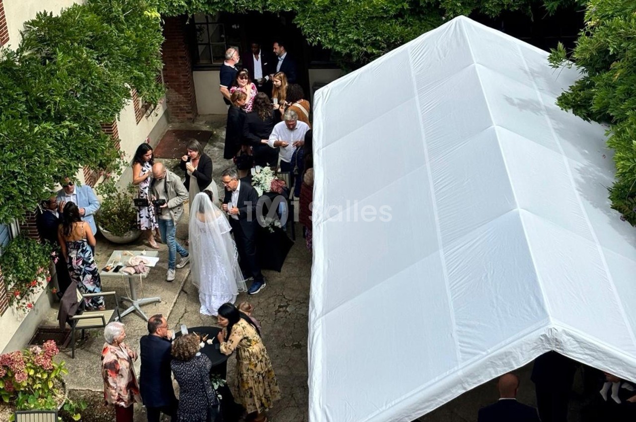 Groupe de personnes rassemblées dans une cour extérieure sous un chapiteau blanc, lors d'un événement festif.