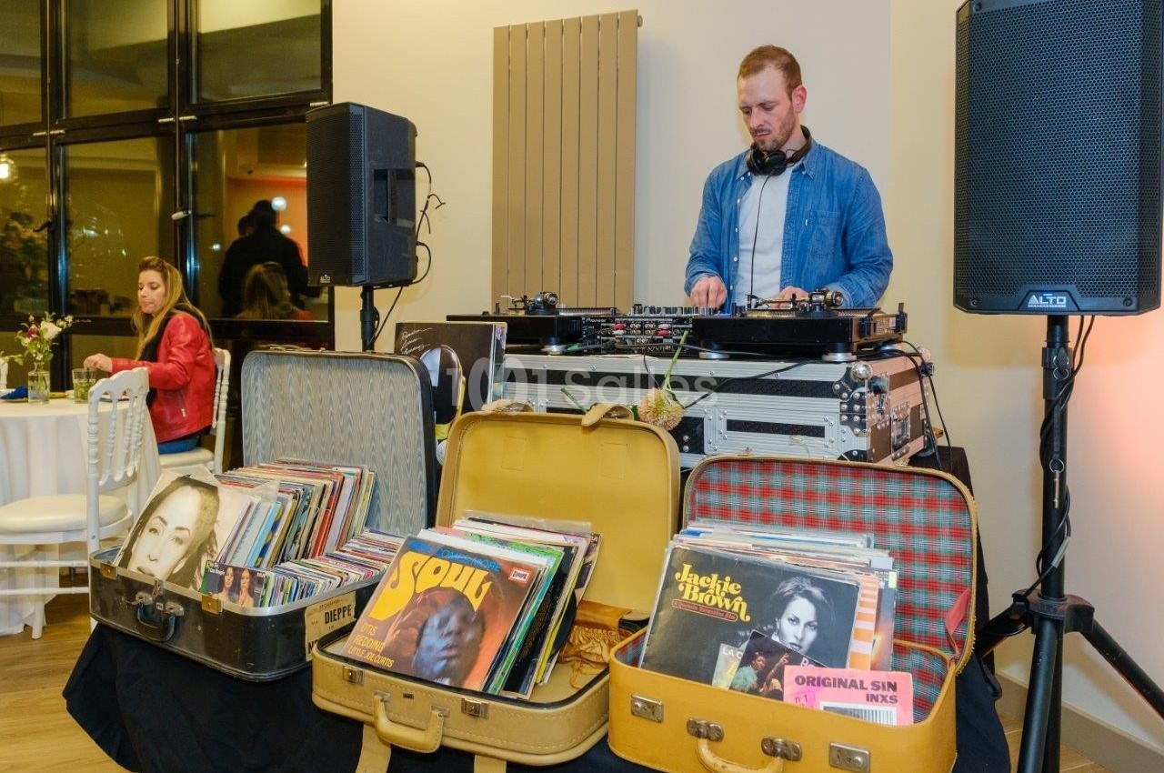 Un DJ mixe de la musique sur une table de mixage, entouré de valises remplies de disques vinyles.