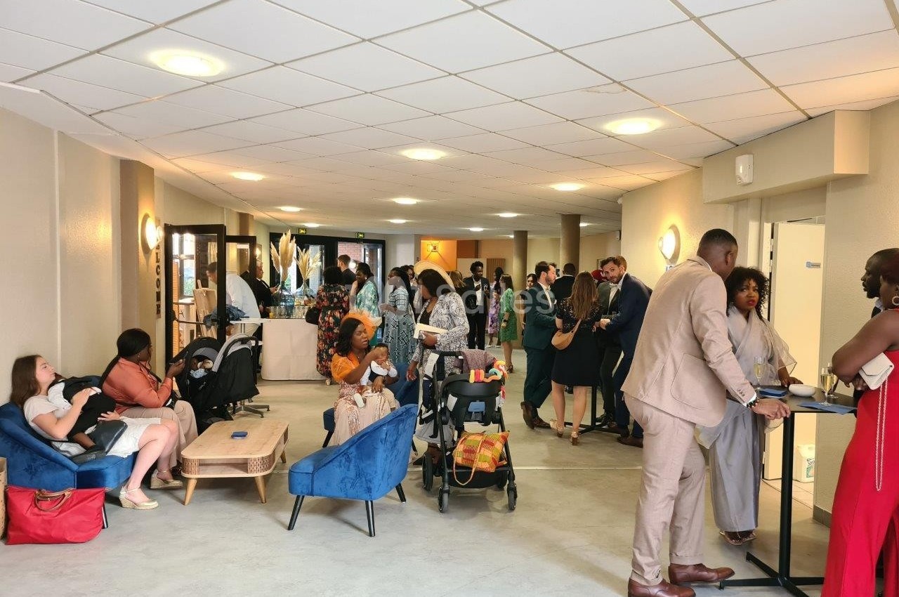 Des personnes discutent et se rassemblent dans un hall lumineux, avec des fauteuils et des poussettes visibles.