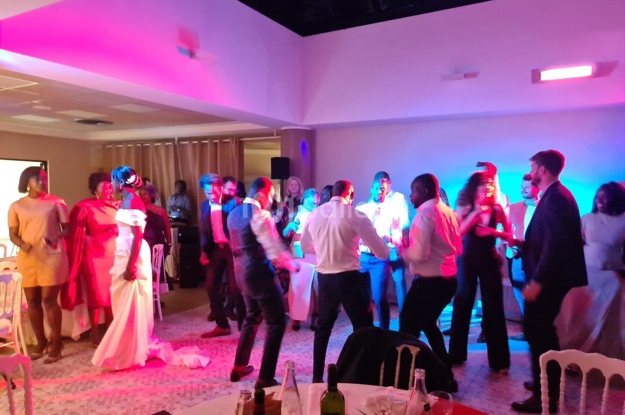 Des personnes dansent et discutent dans une salle éclairée par des lumières colorées, lors d'un événement festif.