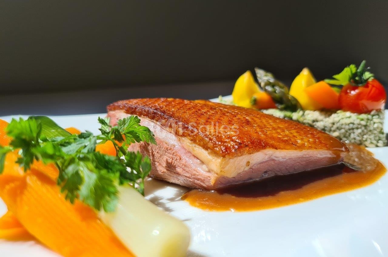 Assiette gastronomique avec magret de canard, carottes, poireau, légumes colorés et sauce, présentée sur une table.