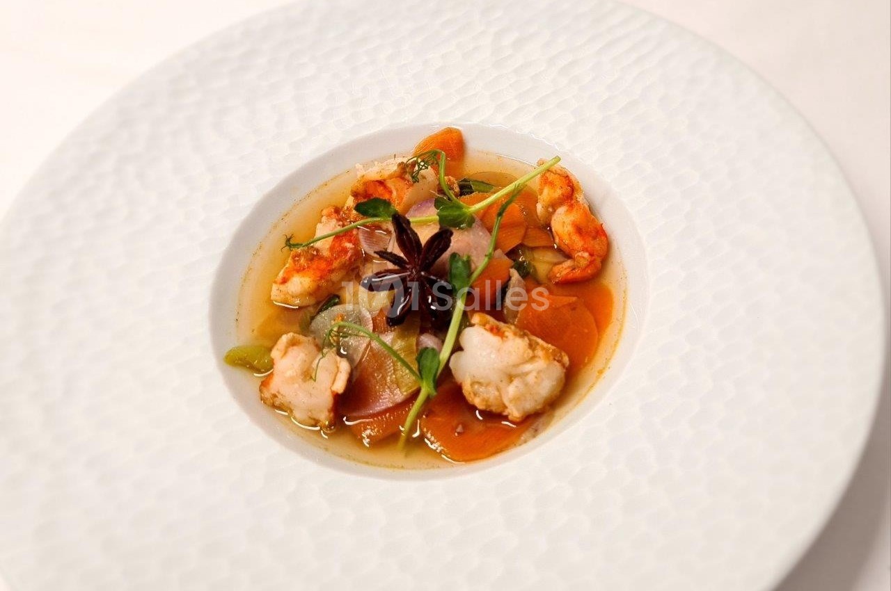 Assiette de soupe raffinée avec gambas, légumes colorés et étoile de badiane en décoration.