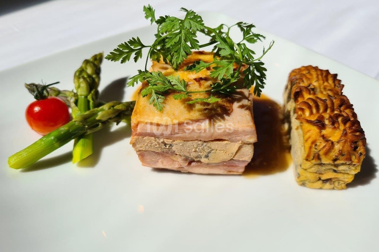 Plat gastronomique composé d'une terrine, d'asperges, d'une tomate cerise et d'un accompagnement gratiné.
