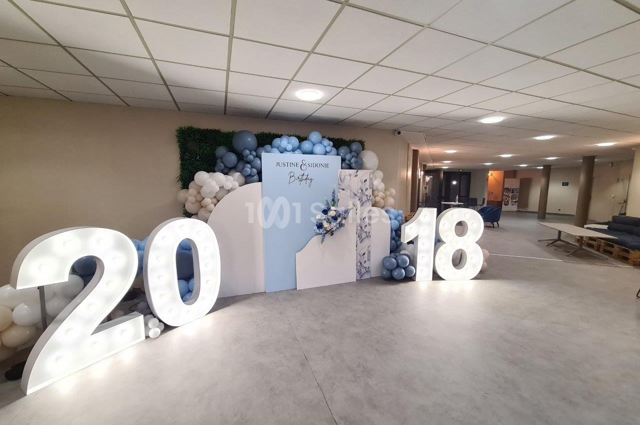 Décoration événementielle avec chiffres lumineux ’2018’, mur de ballons et panneau personnalisé dans une salle éclairée.