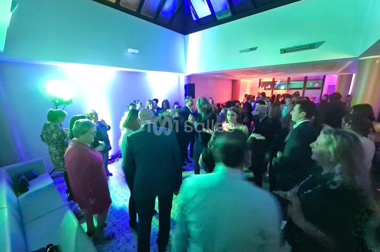 Groupe de personnes dans une salle éclairée par des lumières colorées, discutant et dansant lors d'un événement.