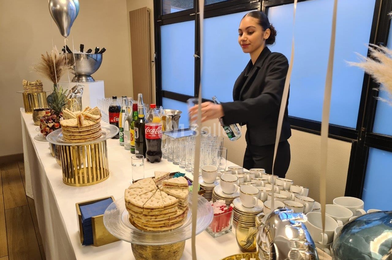 Une femme en tenue professionnelle prépare des boissons sur une table garnie de snacks et de décorations festives.