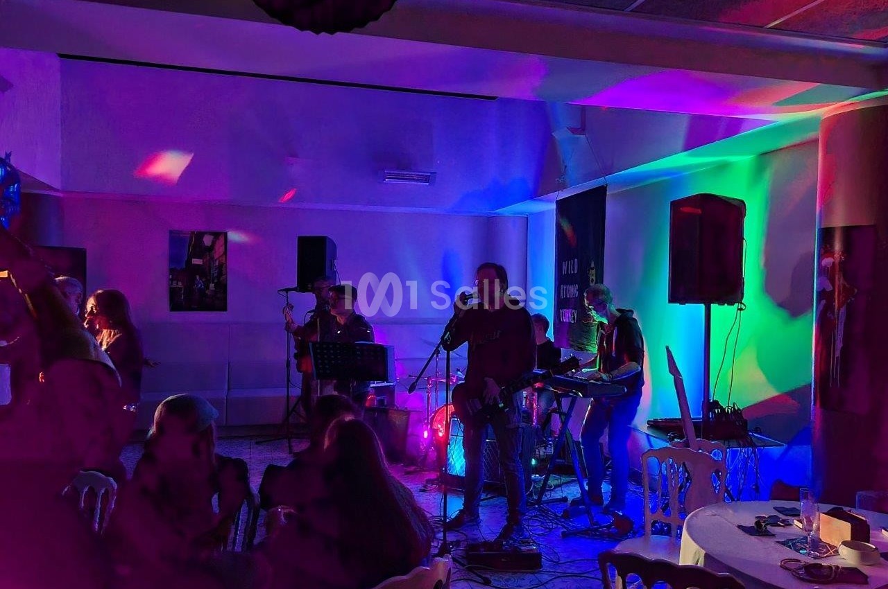 Groupe de musiciens jouant sur une scène éclairée par des lumières colorées dans une salle avec des spectateurs assis.