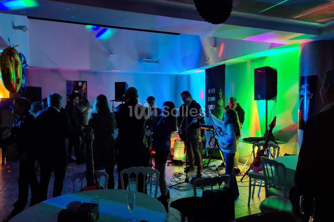 Groupe de musiciens jouant sur scène dans une salle éclairée par des lumières colorées, entourés de spectateurs debout.