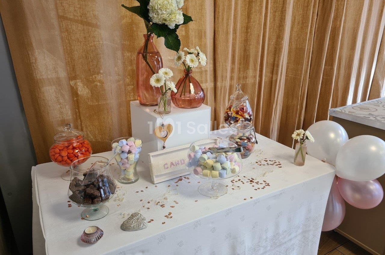 Table décorée avec des bonbonnières remplies de sucreries, des fleurs et des ballons dans un décor chaleureux.