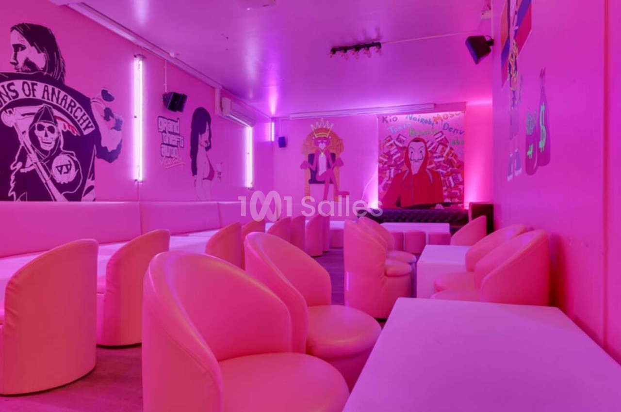 Salle lounge avec fauteuils roses, murs décorés de fresques et éclairage néon rose.