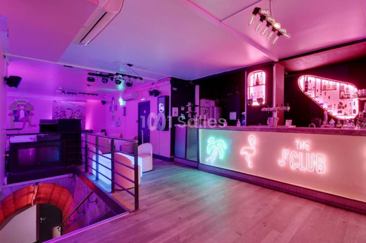 Intérieur d'un bar avec éclairage néon rose et violet, comptoir lumineux et décorations tropicales.