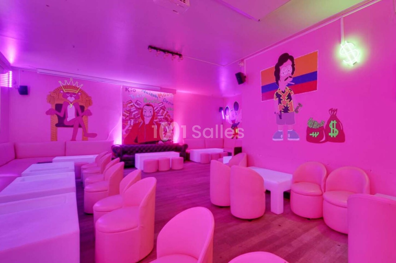 Salle lumineuse avec des murs roses, des illustrations colorées, des néons et des sièges modernes disposés autour de tables…