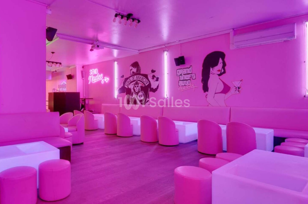 Salle de bar aux murs roses avec banquettes blanches, tabourets assortis et néons décoratifs.
