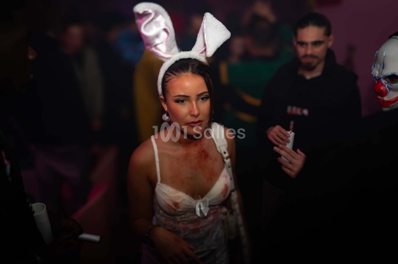 Une femme déguisée en lapin ensanglanté dans une ambiance de fête sombre avec des personnes en arrière-plan.