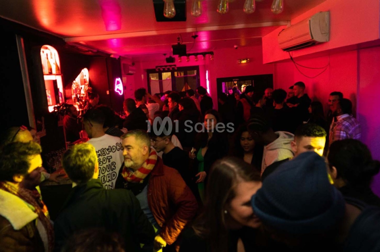 Personnes rassemblées dans un bar ou club, éclairé par des lumières colorées, discutant et profitant de l'ambiance.