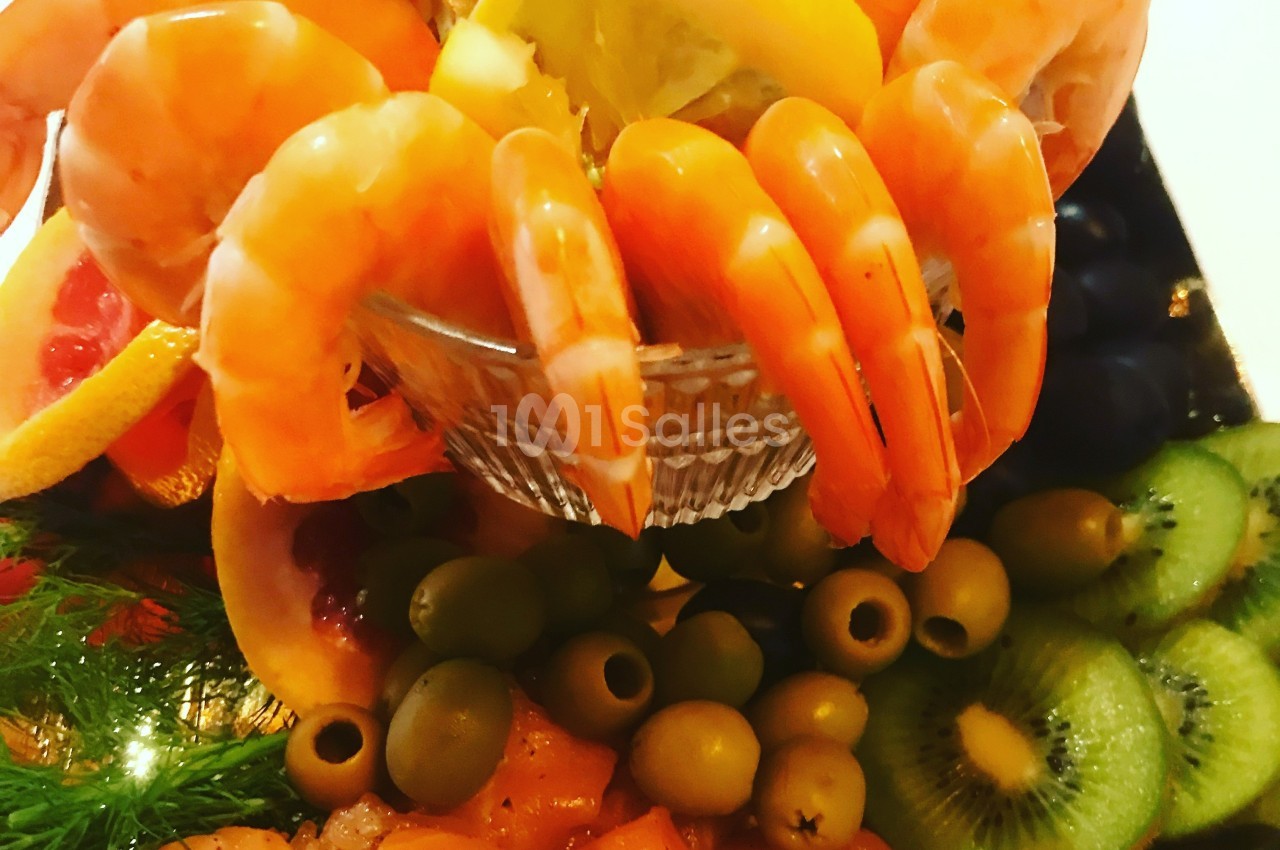 Assiette garnie de crevettes, olives, kiwis, agrumes et autres fruits, présentée dans un bol en verre.