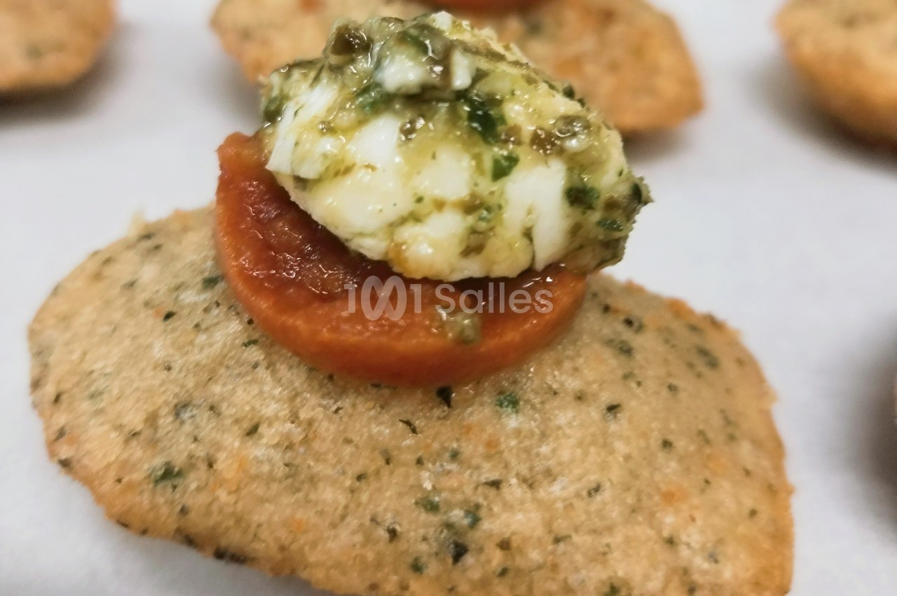 Biscuit salé garni de tomate séchée et fromage frais au pesto, présenté en gros plan.