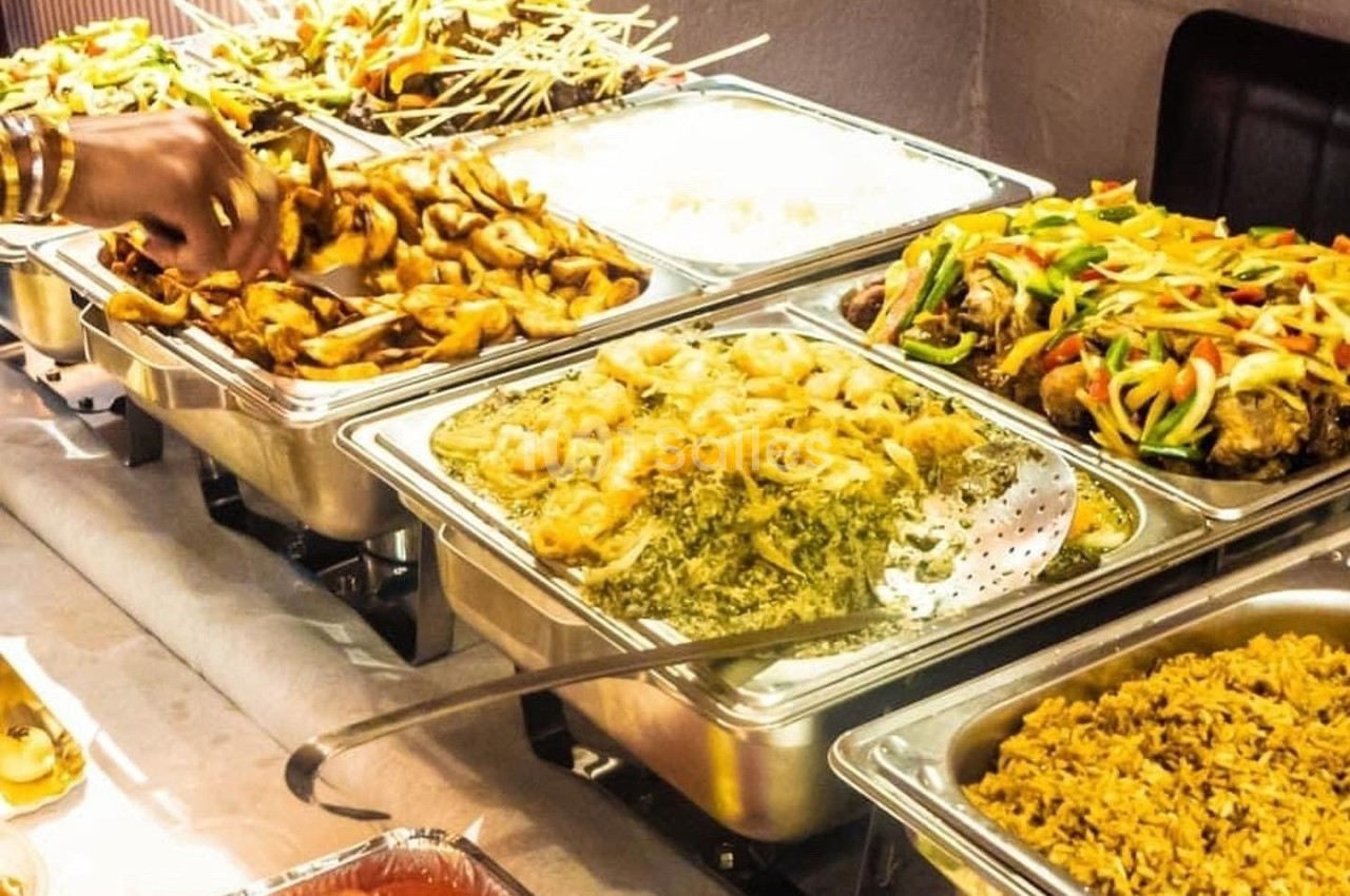 Buffet avec divers plats chauds, dont du riz, des légumes sautés, des brochettes et des préparations à base de viande.