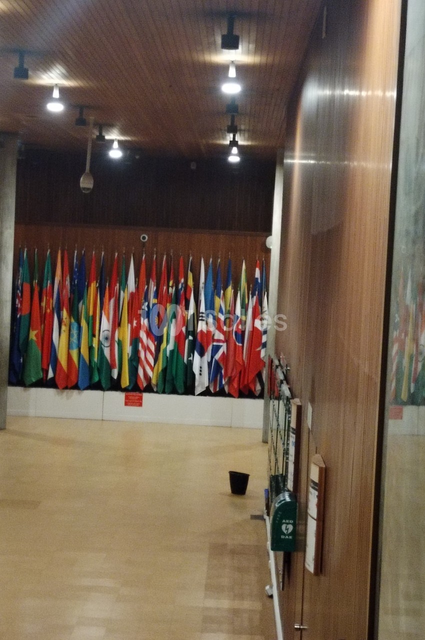 Salle avec un alignement de nombreux drapeaux nationaux, éclairée par des lumières suspendues.