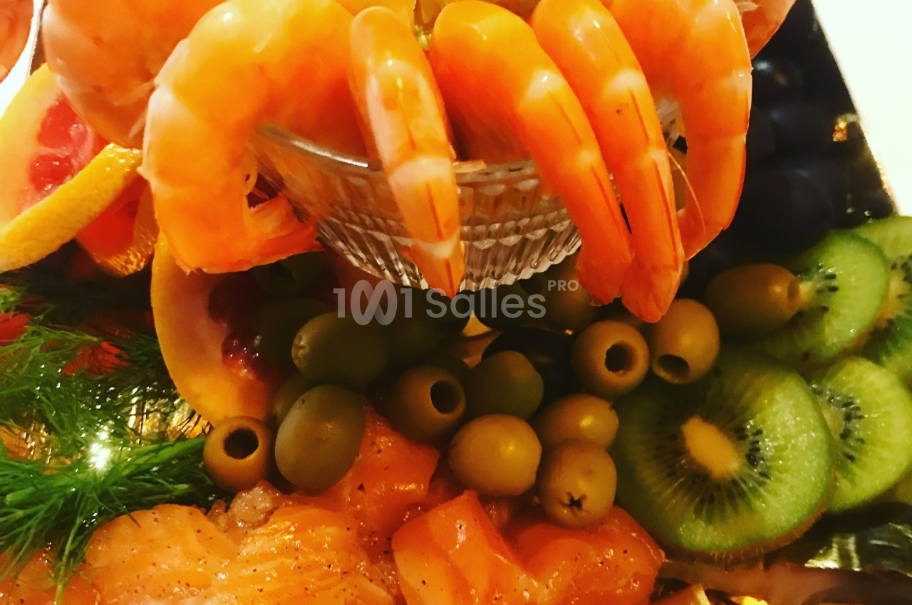 Assortiment de fruits de mer avec crevettes, saumon, olives, kiwis et tranches d'agrumes disposés sur un plateau.