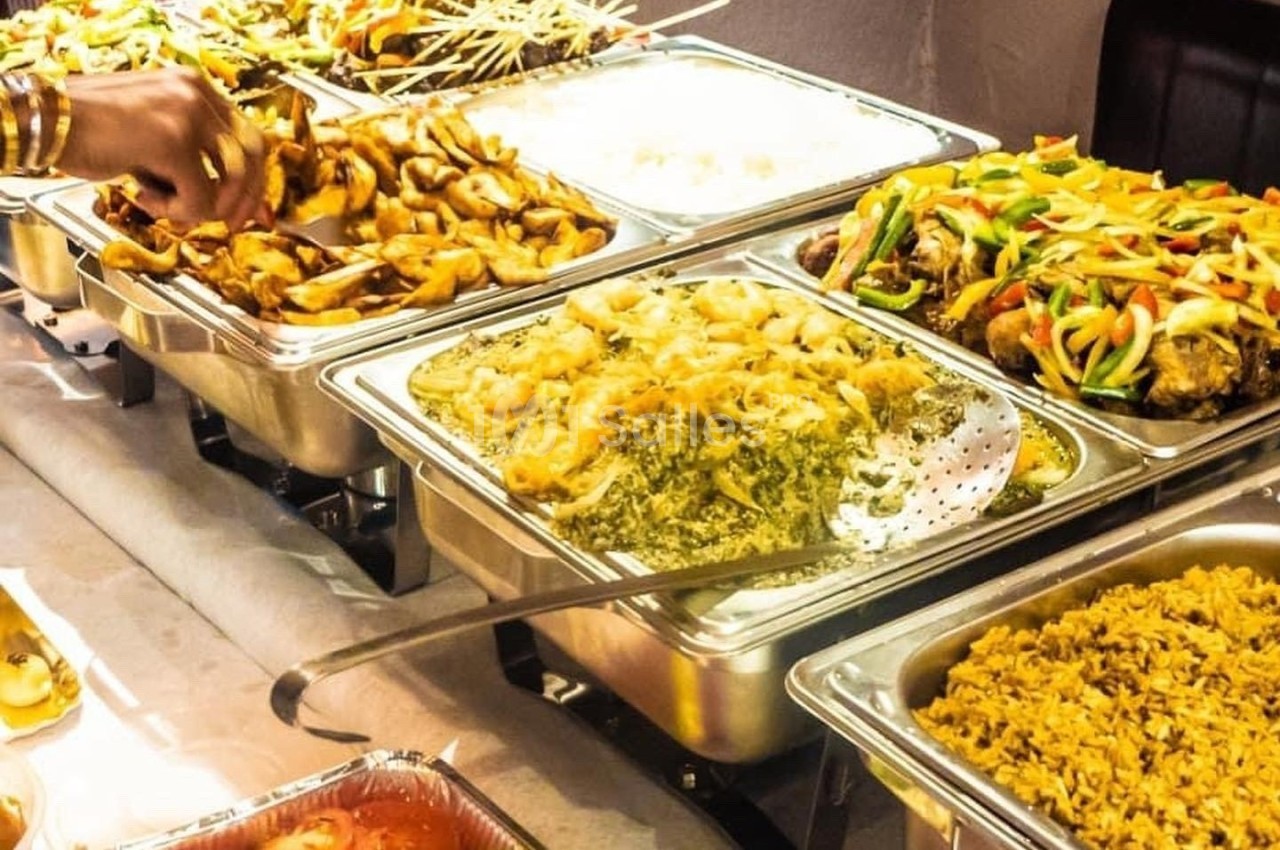 Buffet avec divers plats chauds, incluant du riz, des légumes sautés, des brochettes et des préparations en sauce.